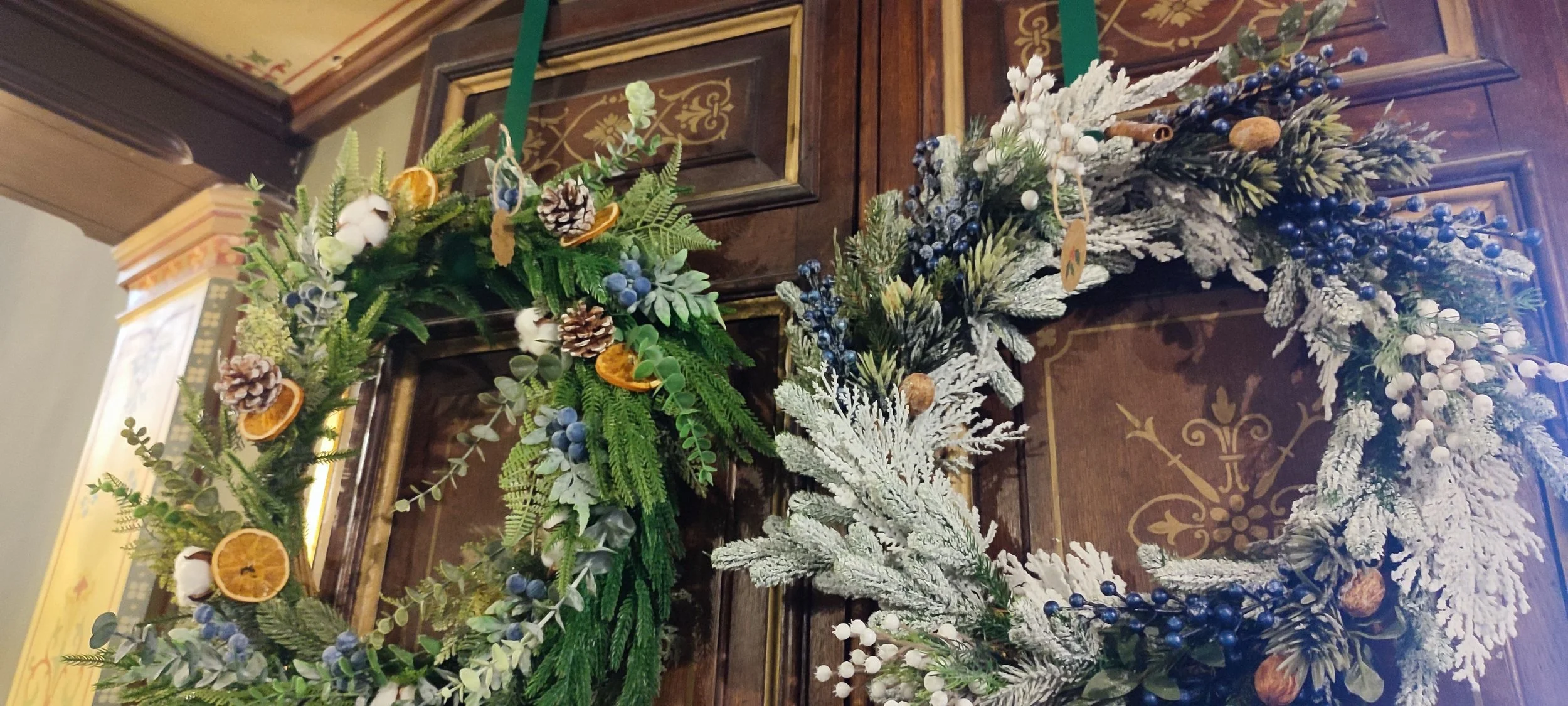 Christmas wreath with greenery, pinecones, dried orange slices, cotton balls, and snowy white branches hanging on a wooden door.