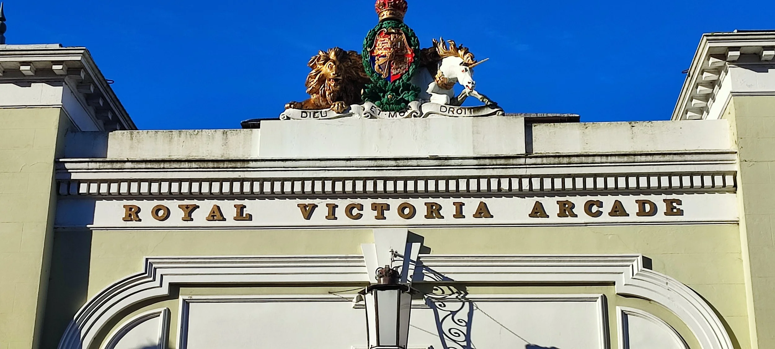 The entrance to the Royal Victoria Arcade with a decorative crest featuring a lion, a unicorn, and a crown on top.