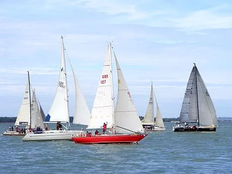 Multiple sailboats sailing on the water with a cloudy sky.