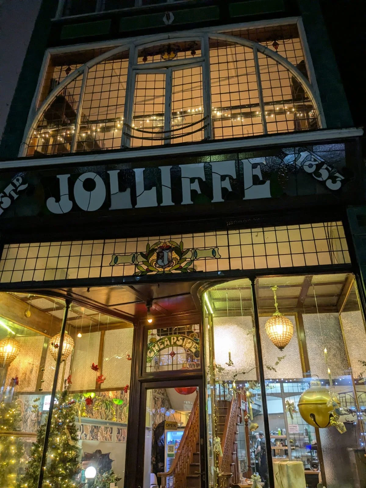 The exterior of a Christmas-themed restaurant or shop decorated with holiday lights, ornaments, and a Christmas tree visible through the glass.