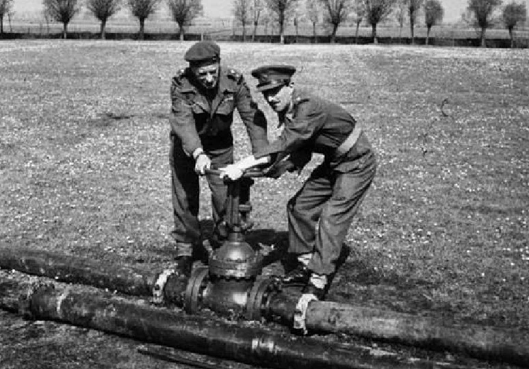 Two men in military uniforms working on a fire hydrant on a sidewalk.