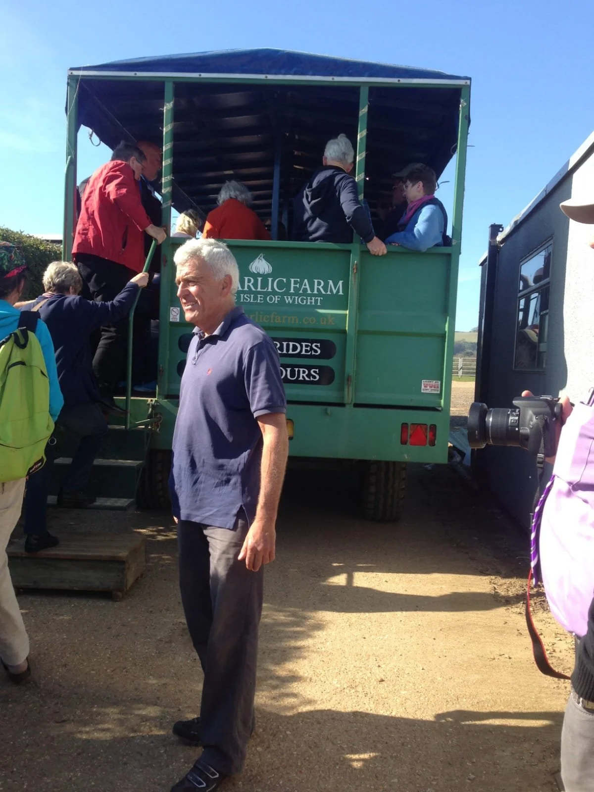 People boarding a green tractor-trailer for guided tours at Garlic Farm on the Isle of Wight on a sunny day.