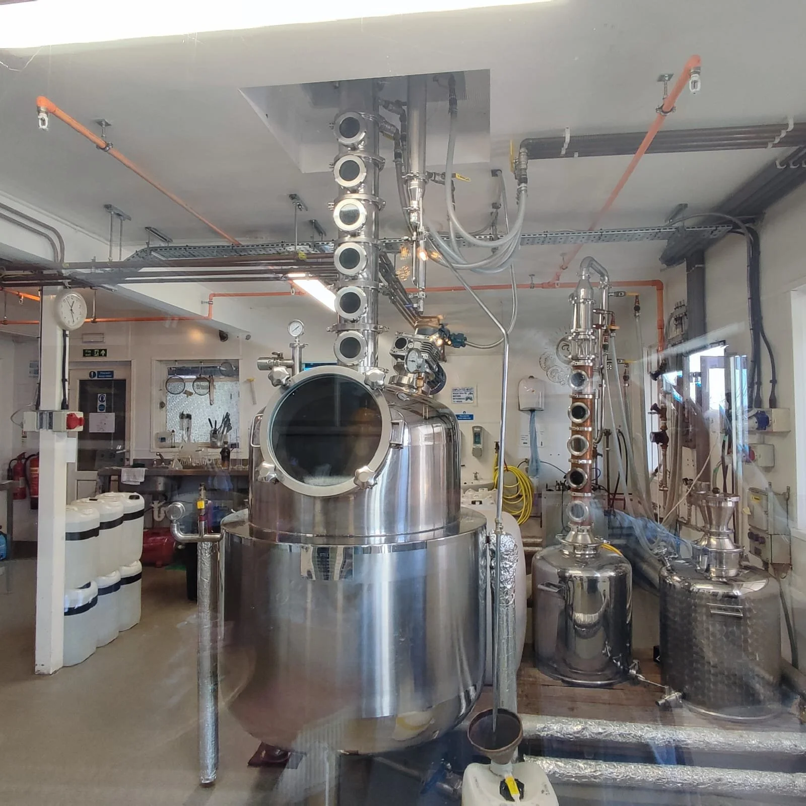 Industrial stainless steel distillation equipment with multiple vertical columns, gauges, and pipes in a laboratory or manufacturing setting.