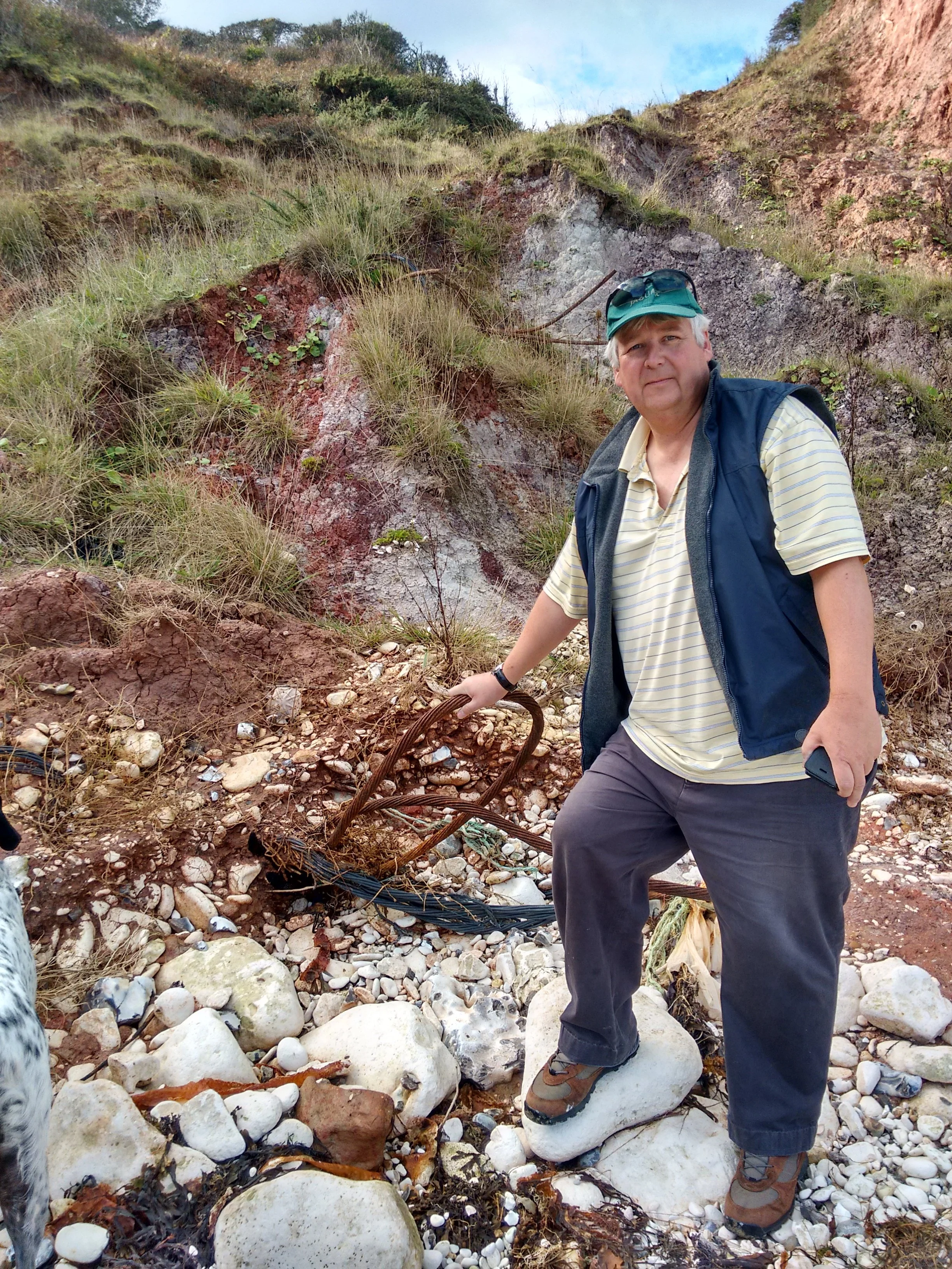 Man standing on a rocky riverbed surrounded by steep, grassy cliffs.