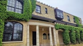Exterior of a yellow brick building covered in green ivy with arched windows and an entrance with stone columns.