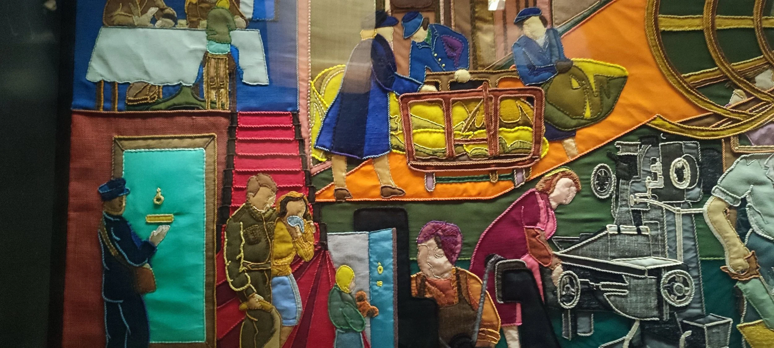 A detailed embroidered patchwork scene illustrating various historical and daily life activities, including people wearing vintage clothing, a train, and buildings.