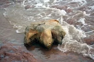 A large rock on a shoreline with waves washing over it.