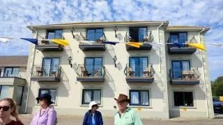 Four people standing outside a residential building with balconies featuring yellow umbrellas.