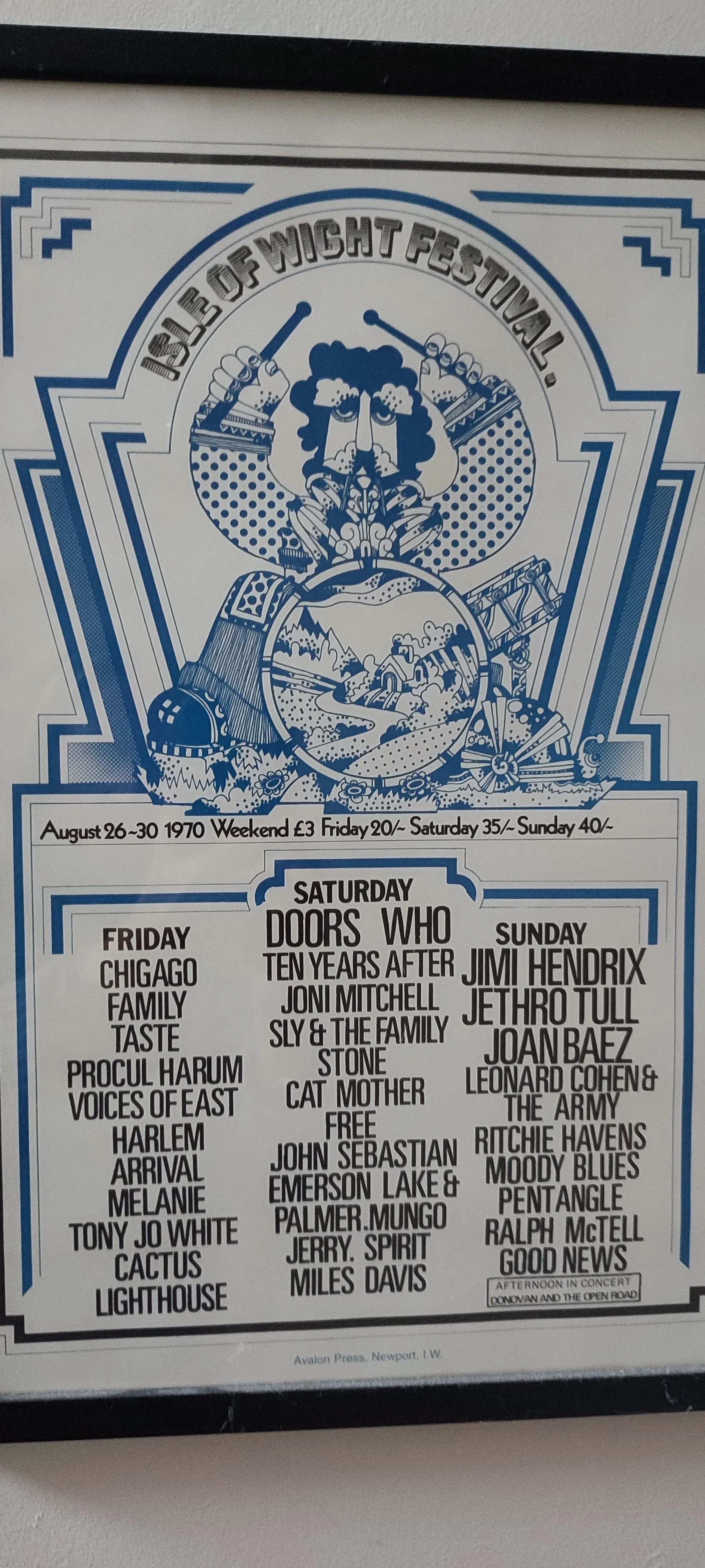 A poster for the Isle of Wight Festival, 1970, with a blue and white graphic design. The poster features a large illustration of a person with curly hair, holding drumsticks, surrounded by musical and festival imagery. It lists bands and performers for each day, including Chicago, Family, Taste, Procol Harum, Voices of East, Harlem, Arrival, Melanie, Tony Joe White, Cactus, Lighthouse, Doors, Who, Jimi Hendrix, Joni Mitchell, Sly & the Family Stone, Cat Mother, John Sebastian, Emerson Lake & Palmer, Jerry Garcia, Miles Davis, Joan Baez, Leonard Cohen & The Army, Ritchie Havens, Moody Blues, Pentangle, Ralph McTell, and Good News, scheduled from August 26-30, 1970.