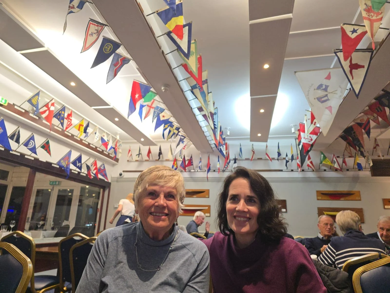Two women sitting at a table in a room decorated with colorful flags hanging from the ceiling.