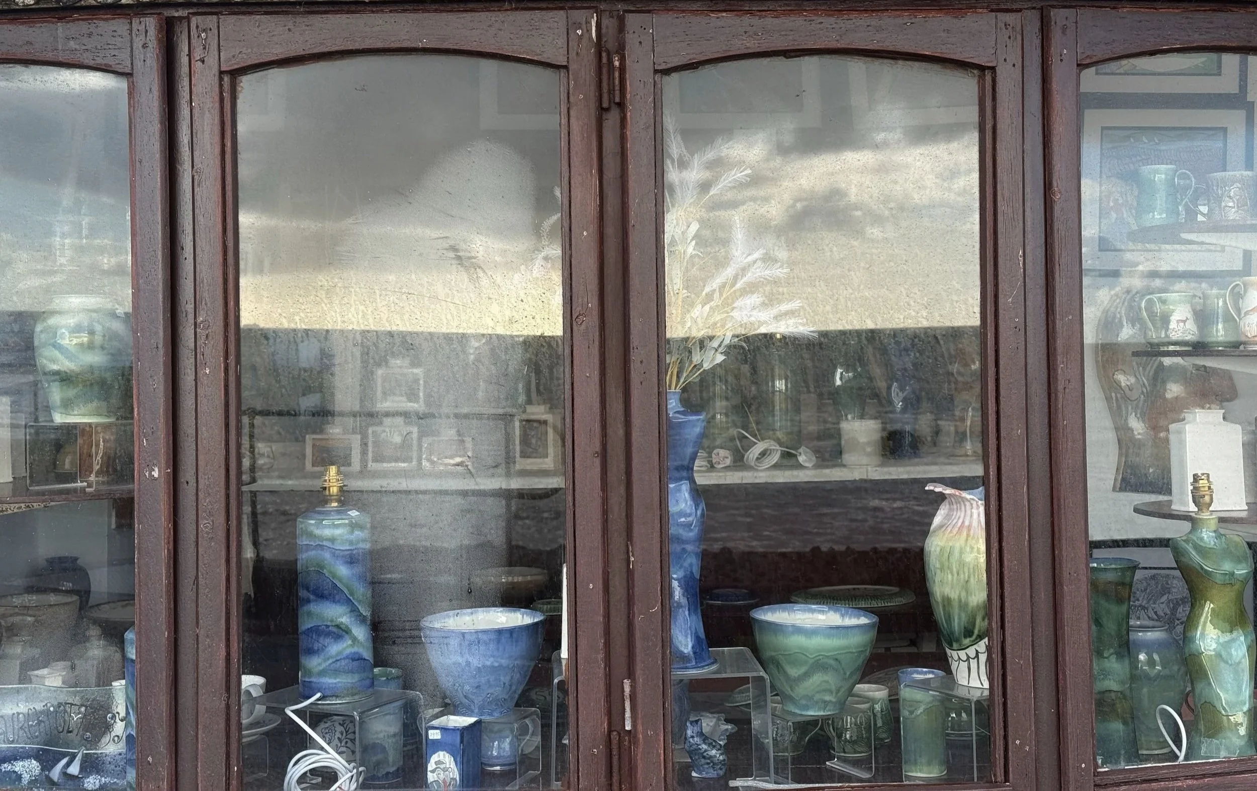 A wooden display cabinet with glass doors showing various vases and bowls inside, some with blue, green, and beige colors.