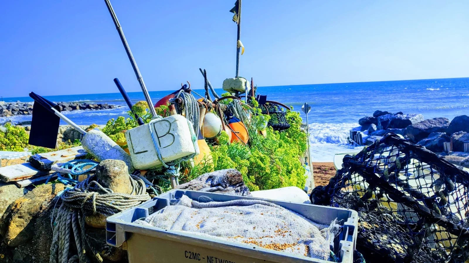 Collection of fishing gear and buoys on a rocky beach with ocean and sky in the background