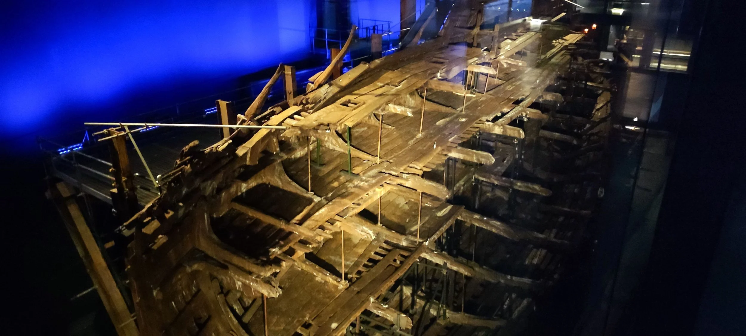 A wooden model of Noah's Ark displayed in a dimly lit exhibition with blue lighting in the background.
