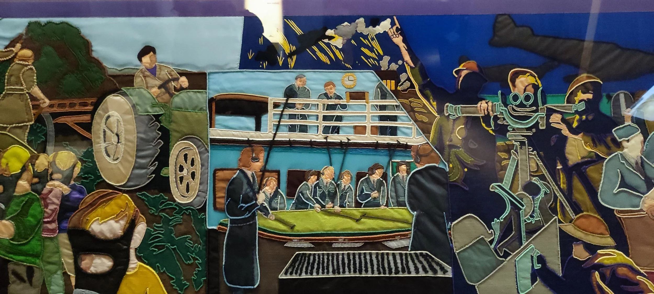 A fabric collage depicting a train with passengers, a cyclist, and a camera crew, with a background of storm clouds and lightning.