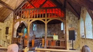 View of an indoor stage with wooden balcony, stone walls, and musical equipment, inside a rustic church or hall.