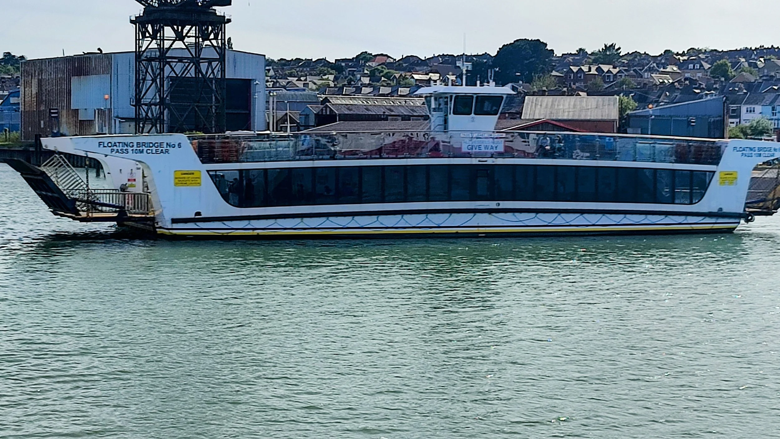 A white passenger ferry boat on a body of water near a town with buildings and houses in the background.