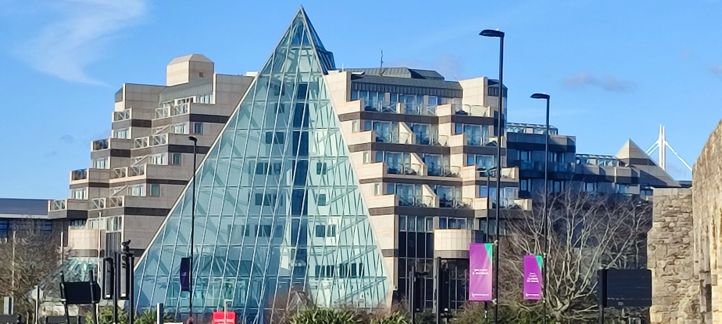 Modern glass pyramid structure surrounded by residential buildings and streetlights under a blue sky.