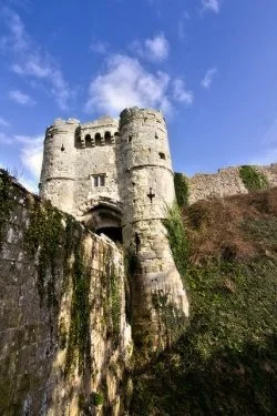 A medieval stone castle with turrets and a drawbridge, set on a hill under a blue sky with some clouds.