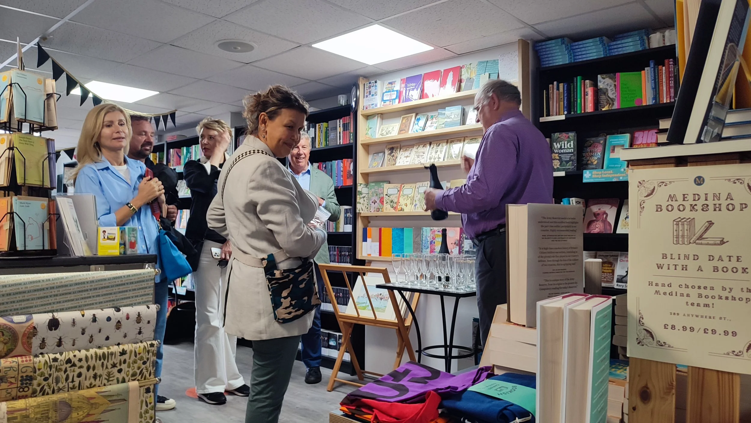 A group of people inside a bookstore, engaging in a book signing event. A woman is signing a book for a man, while others wait in line behind them.