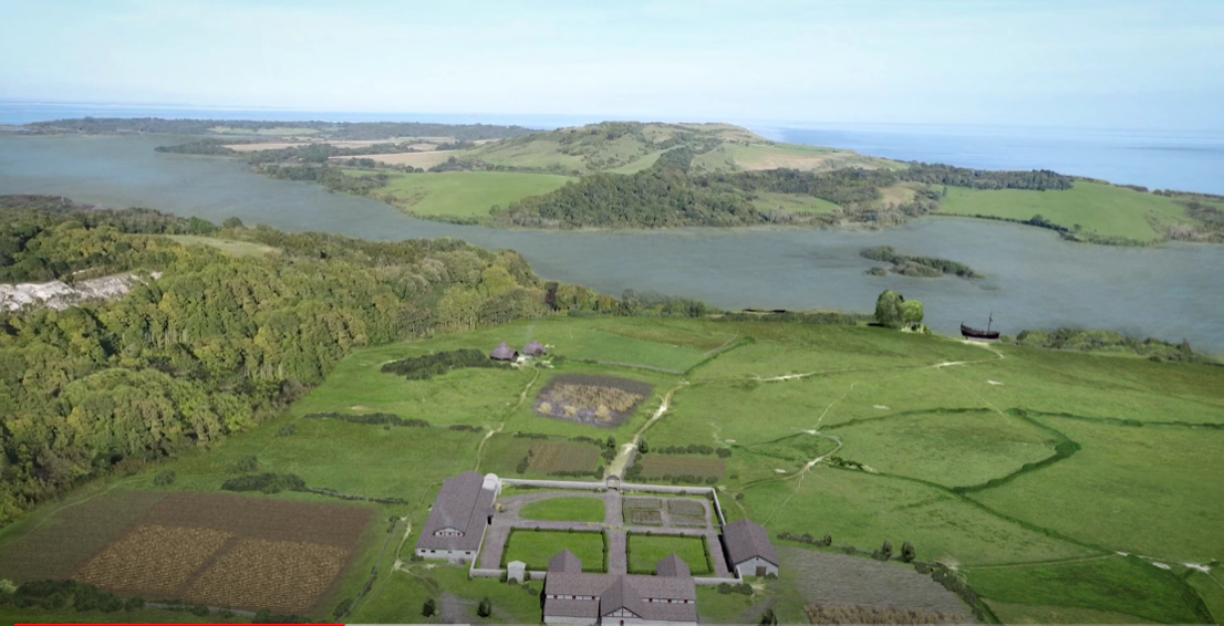 Aerial view of green farmland with fields, wooded areas, and a few buildings, overlooking a large body of water with small islands and shorelines in the background.