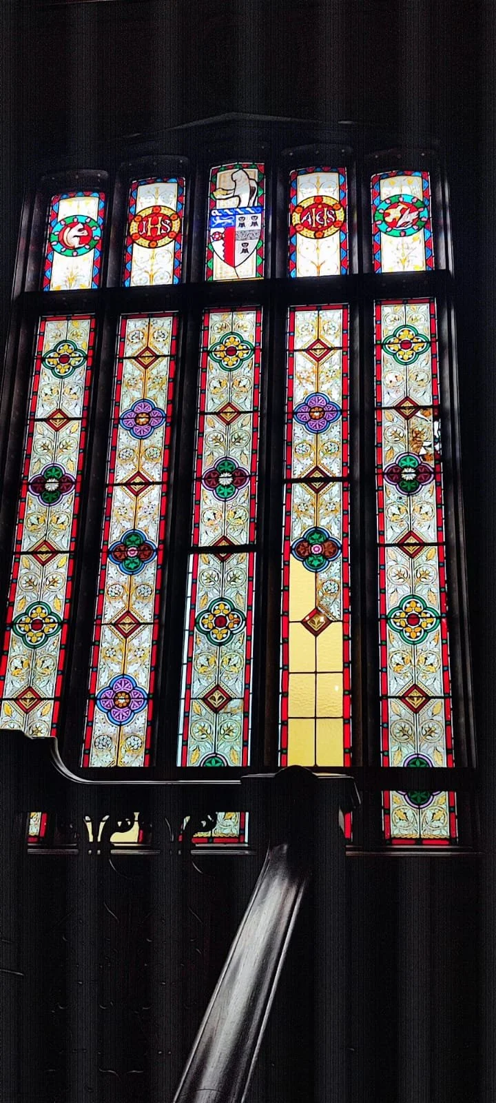 Colorful stained glass window depicting religious symbols and floral patterns, with wooden handrail in foreground.