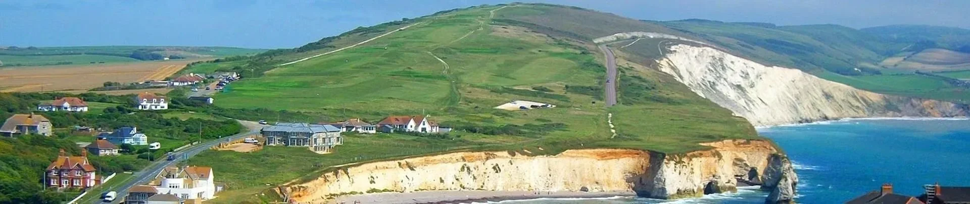 Coastal landscape with green hills, white cliffs, a beach, and the ocean under a cloudy sky.
