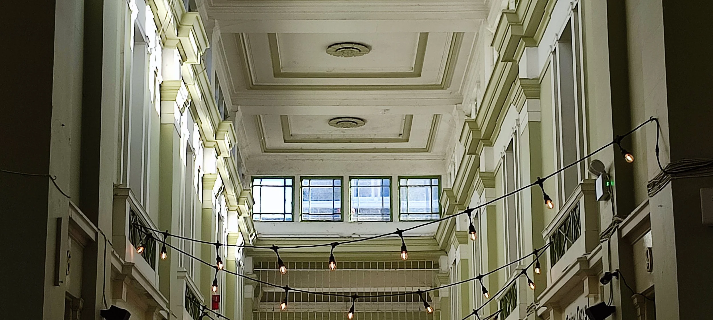 Interior of a multi-story building with a high ceiling, large windows at the top, and hanging string lights with bulbs.