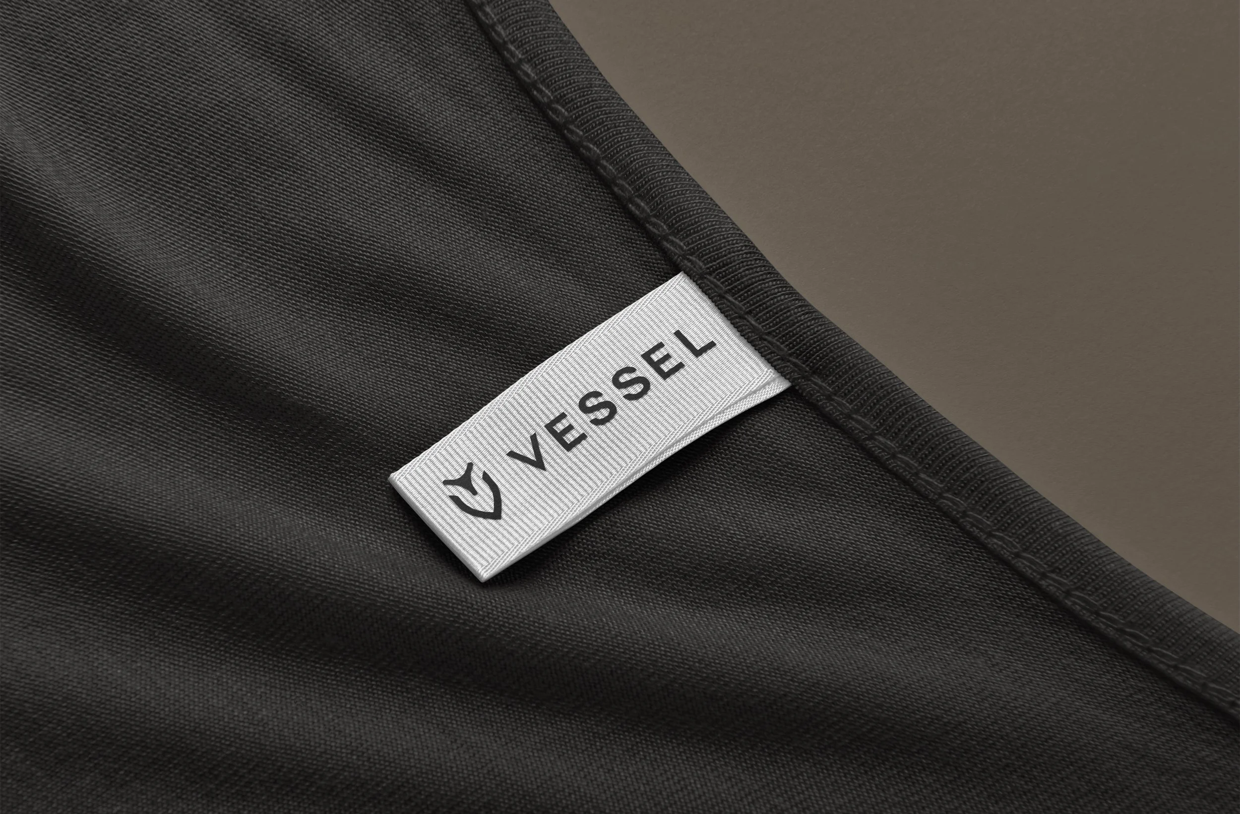 Close-up of a black fabric with a white label that says 'Vessel' and features a small logo, along a seam.