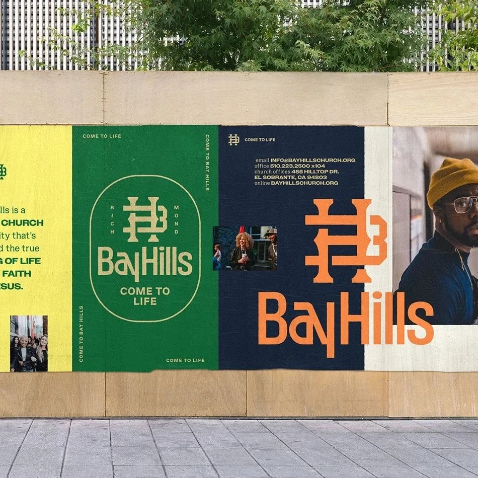 A colorful outdoor banner for Bay Hills church with the logo, contact information, and photographs, mounted on a wall with trees and a fence in the background.