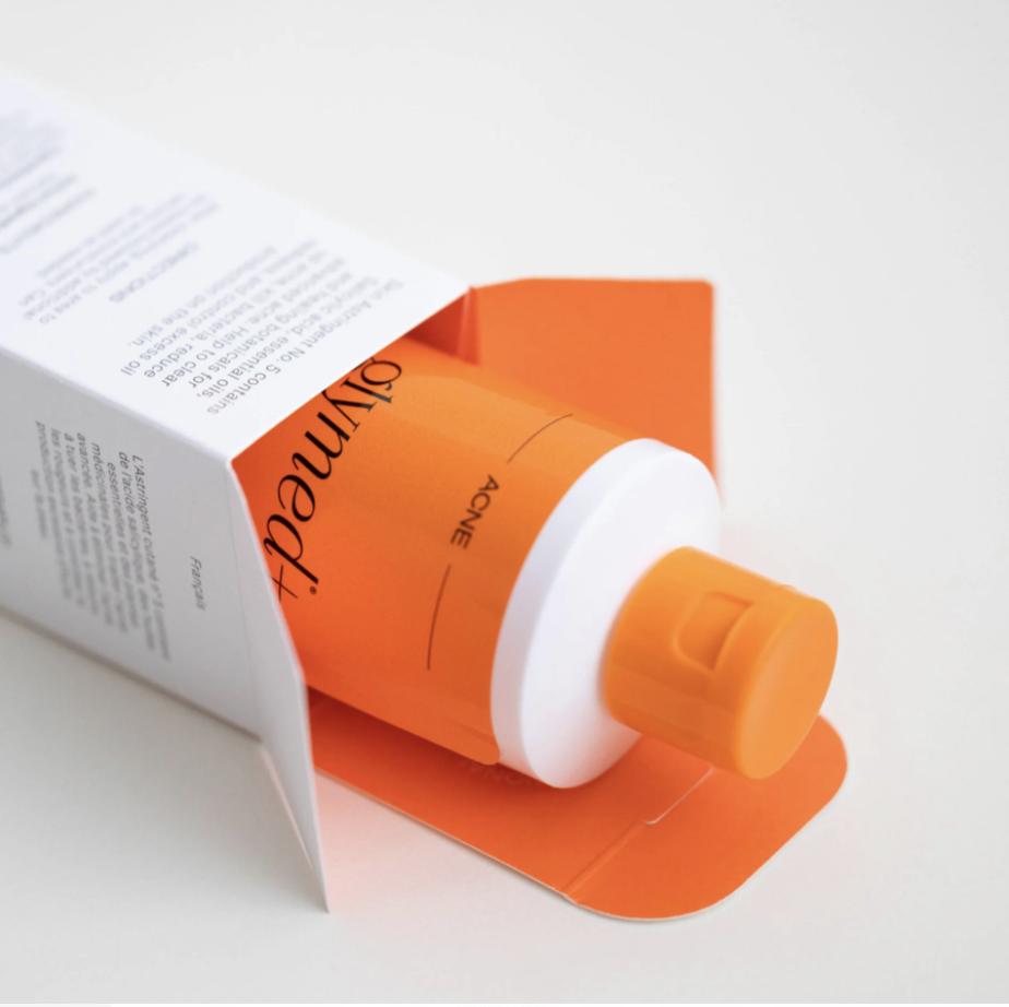 A partially opened orange and white bottle of sunscreen inside an orange and white paper sleeve on a white surface.