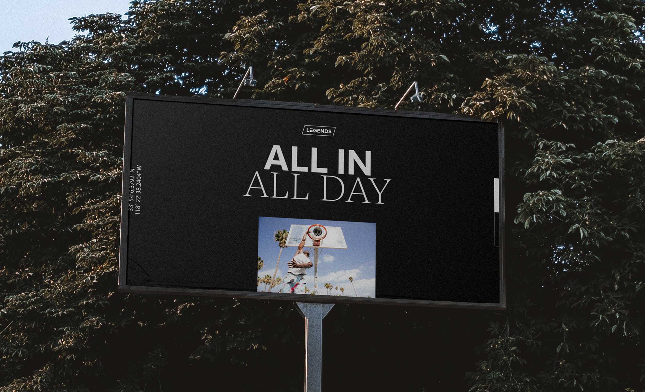Outdoor billboard with black background displaying the text 'ALL IN ALL DAY' in large white letters, with a small image of a person dunking a basketball at a hoop, palm trees, and blue sky in the background.