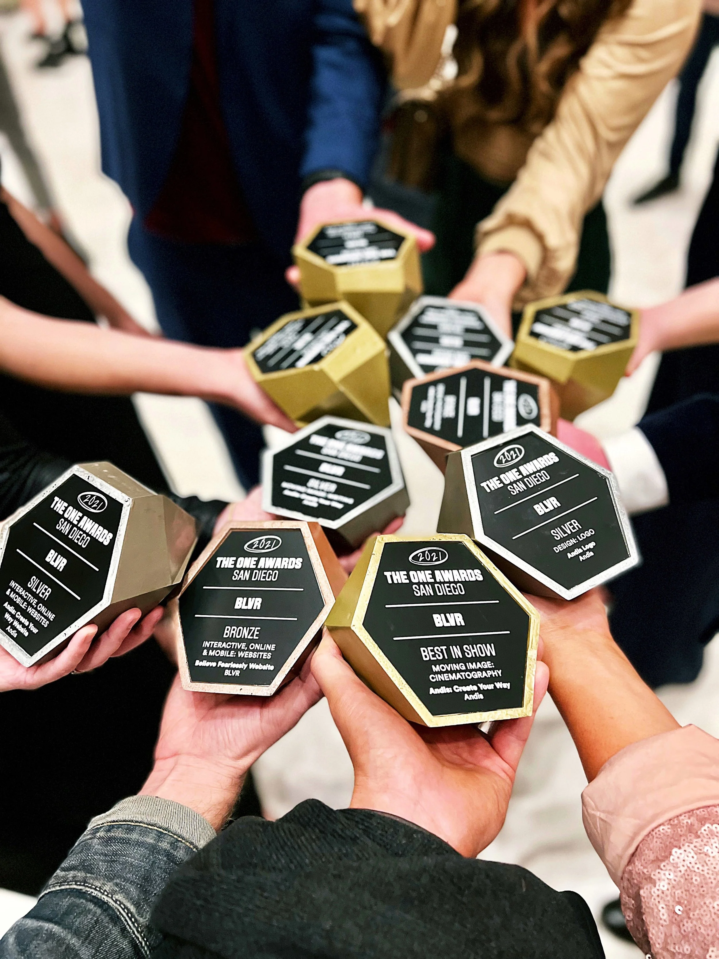 Group of people holding up trophies with black labels, celebrating an awards event at The One Awards in San Diego.