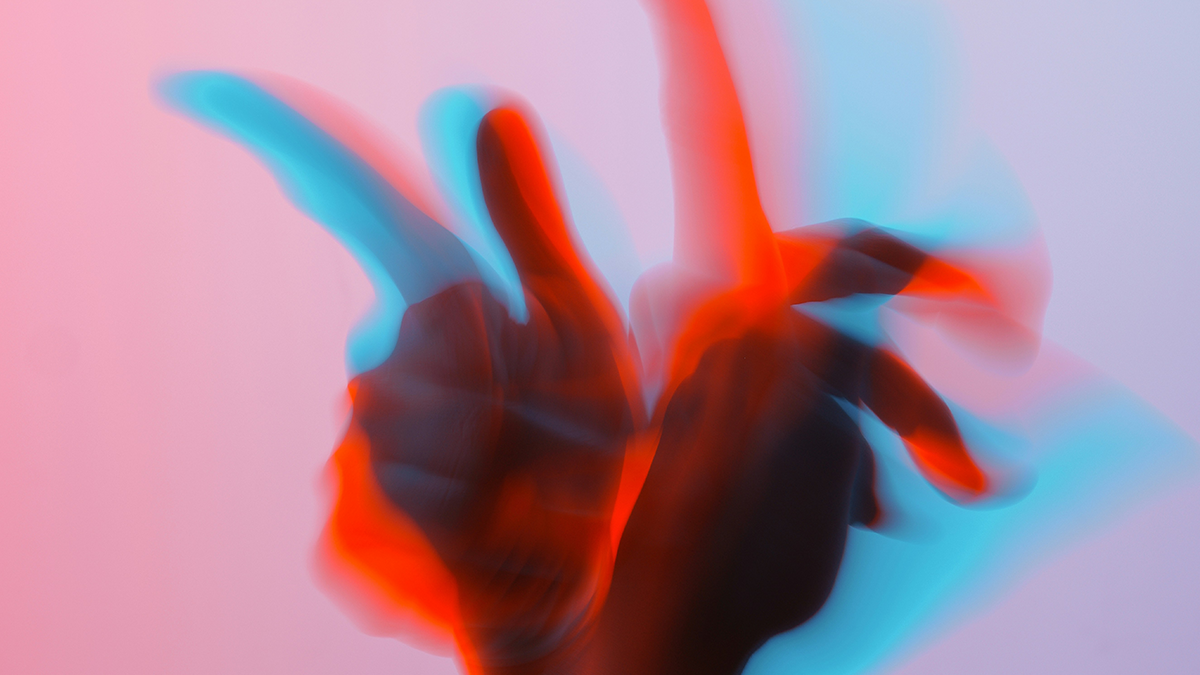 Blurred hand making a peace sign with neon red and blue lighting against a pastel background.