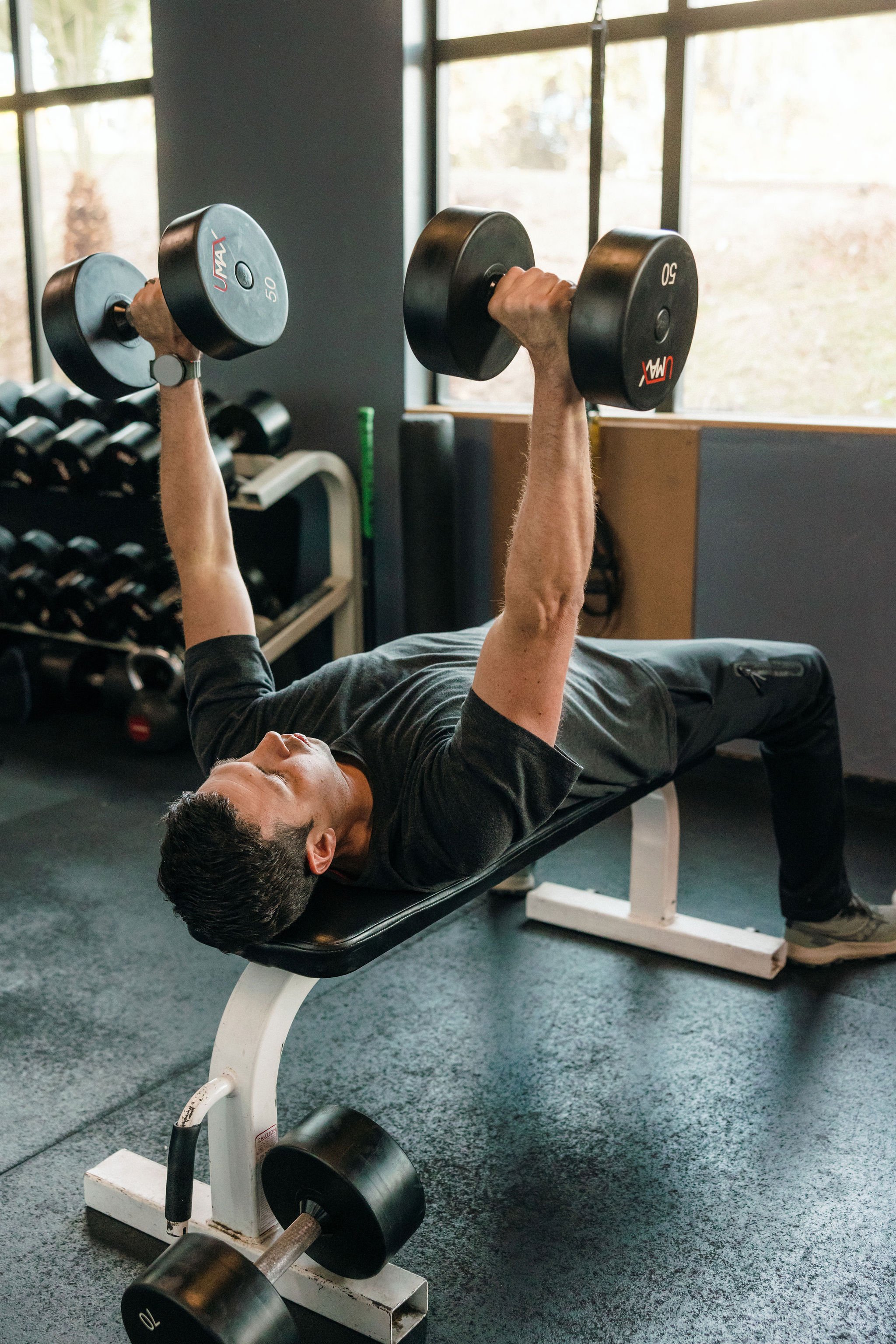 Man lifting dumbbells in a gym as part of a disciplined physical practice connected to the 100xLife challenge.