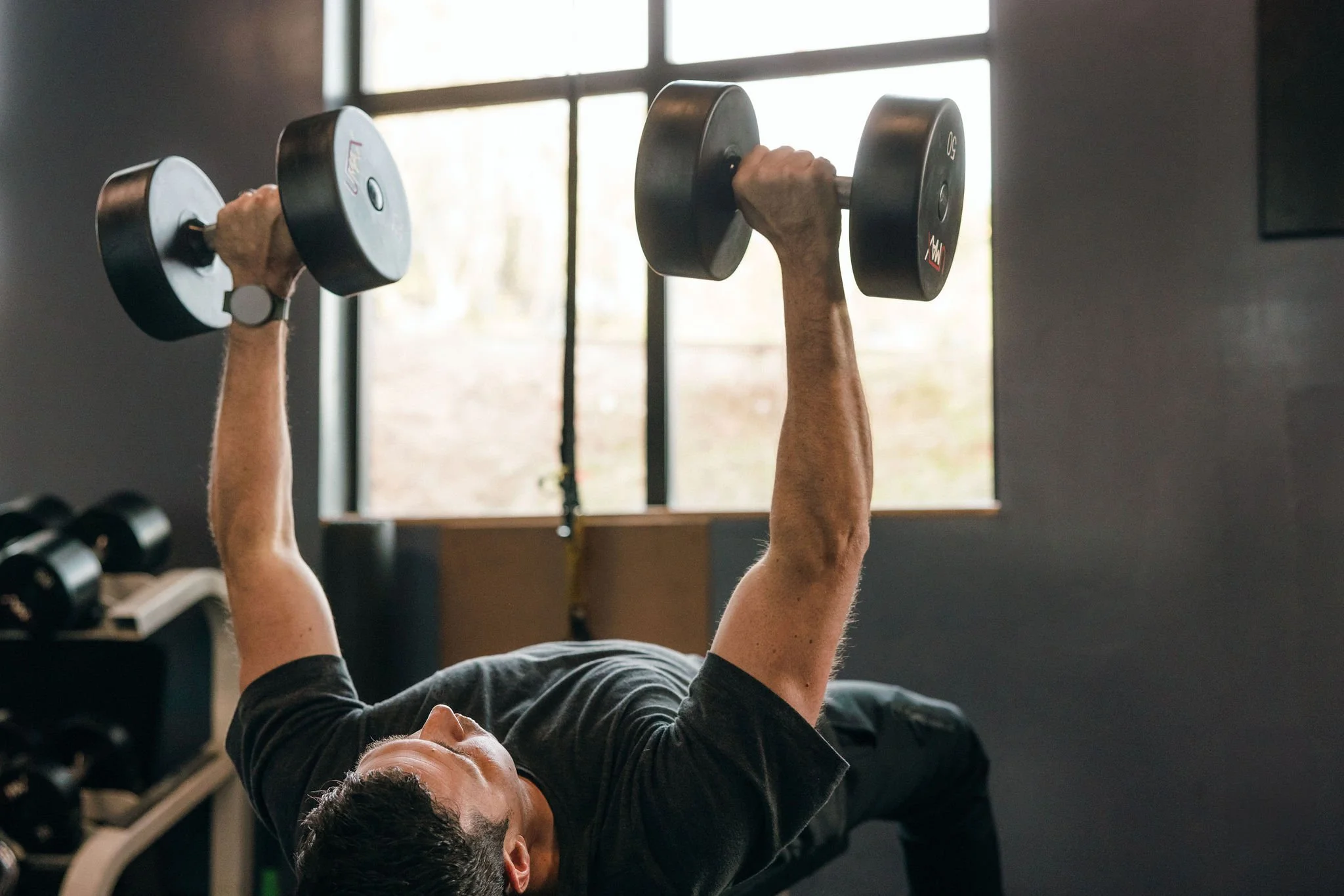 Person lifting dumbbells in a gym as part of a disciplined physical practice.