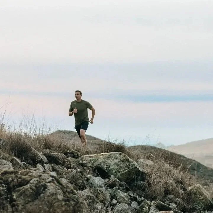 A man running on a rocky trail on a hillside as part of a disciplined movement practice.