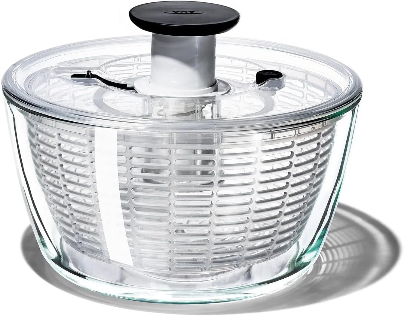 A clear glass salad spinner with a black lid and a black handle, placed on a white background.