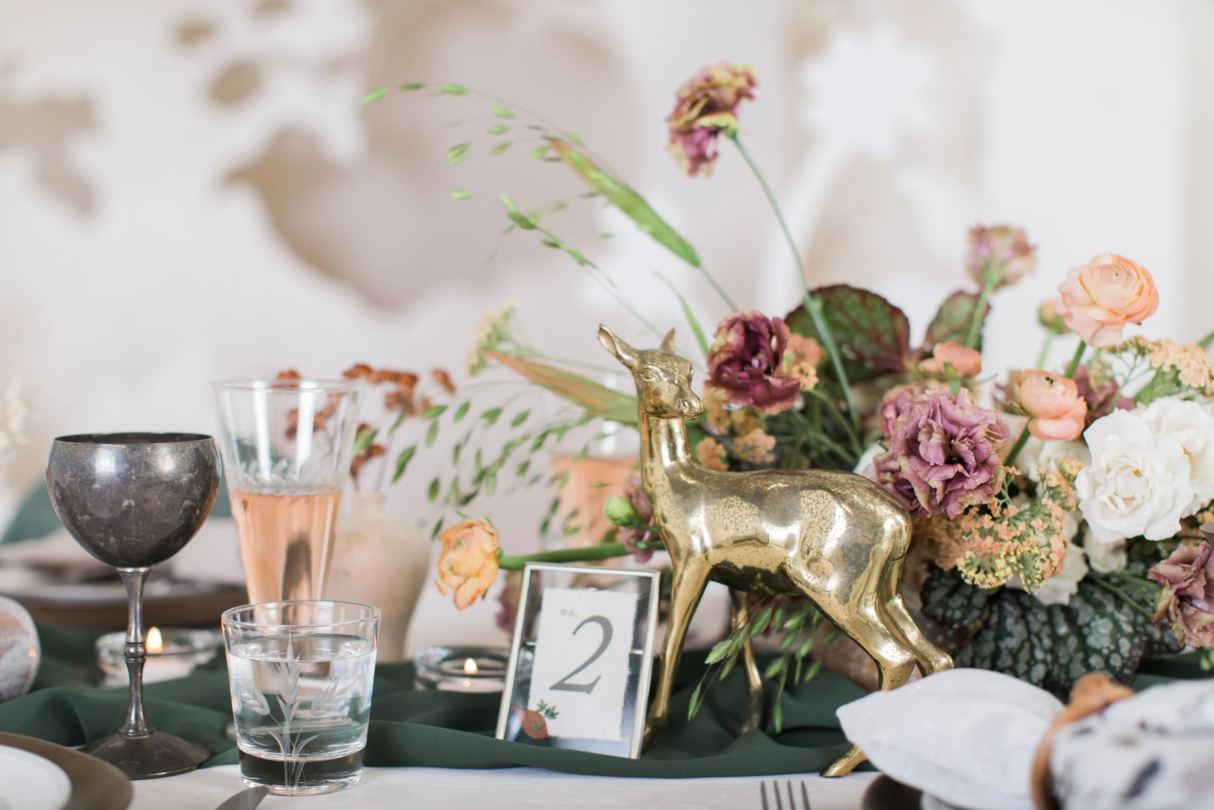 Fall wedding table centerpiece with gold deer, forest green runner, and mauve floral accents