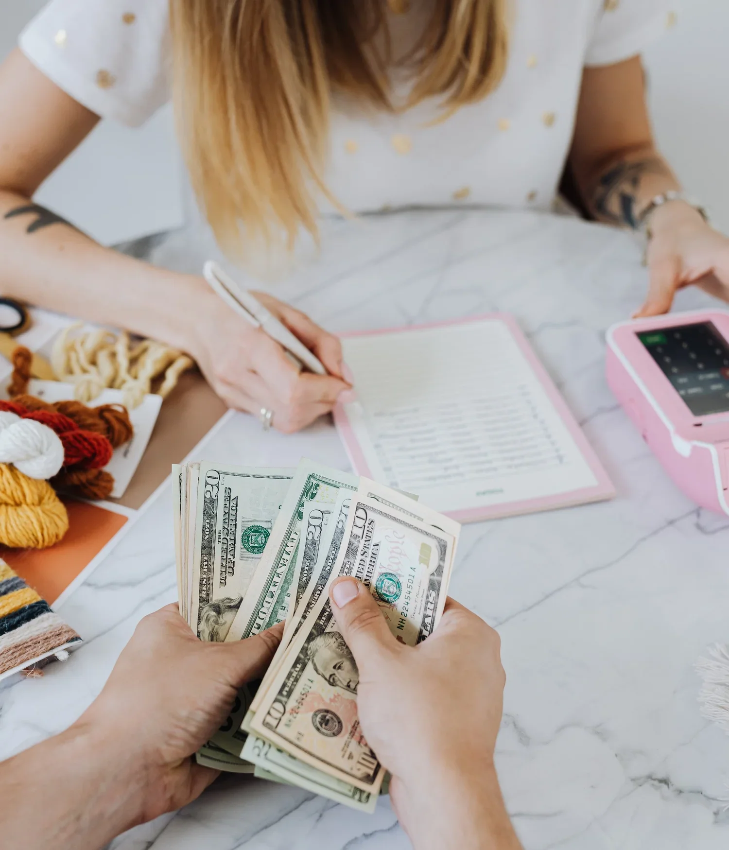 Hands counting cash and reviewing a wedding planning checklist with colorful craft supplies