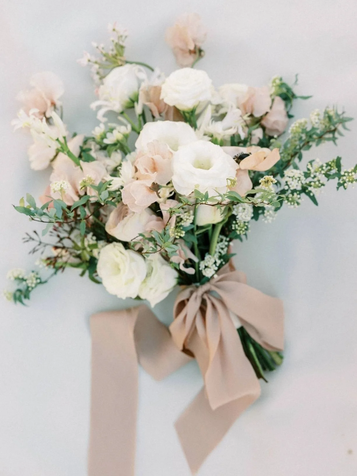 Elegant bouquet of white and pale pink flowers tied with a beige ribbon, on a white background.