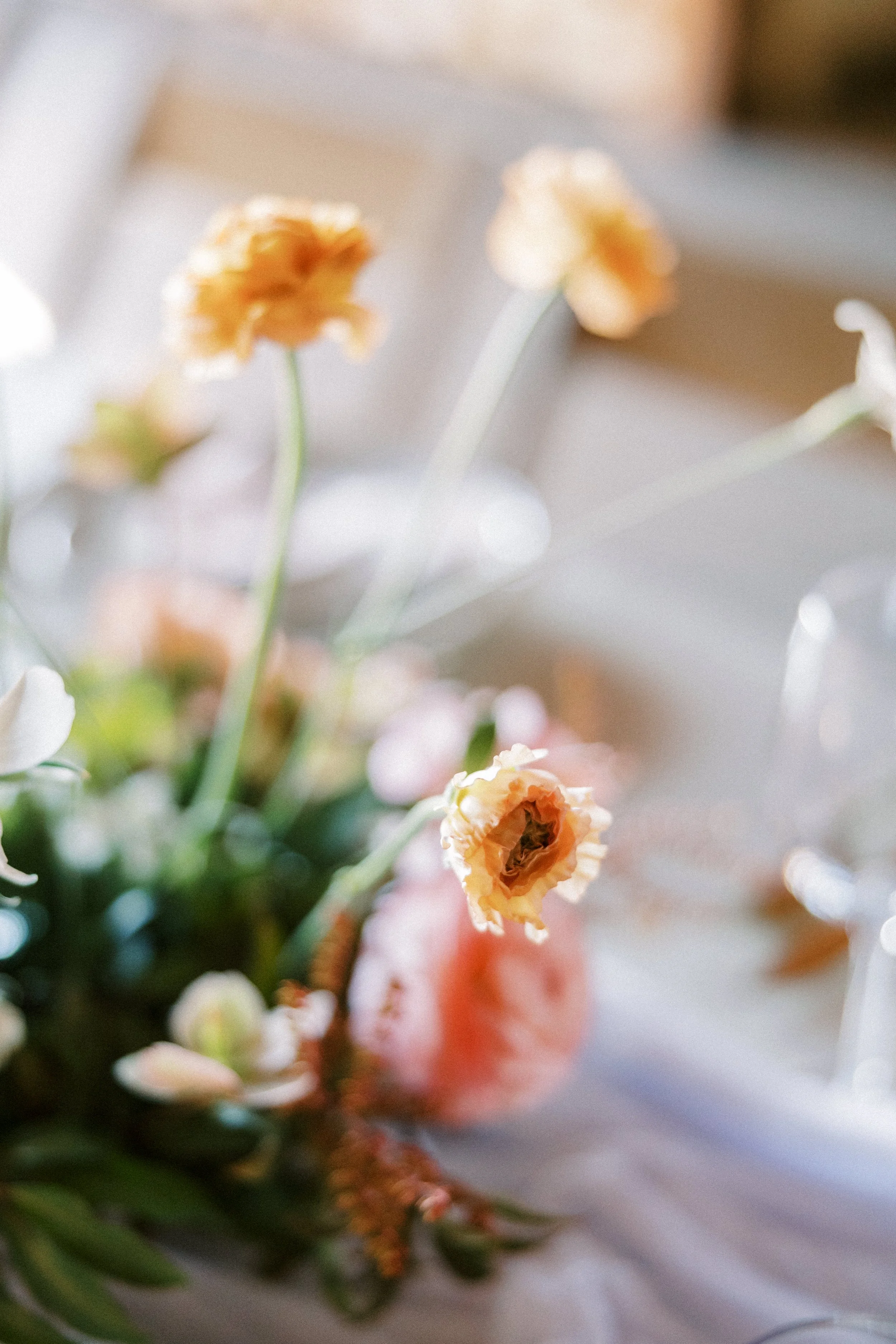 Close-up of a bouquet with peach-colored and white flowers on a table with glassware.