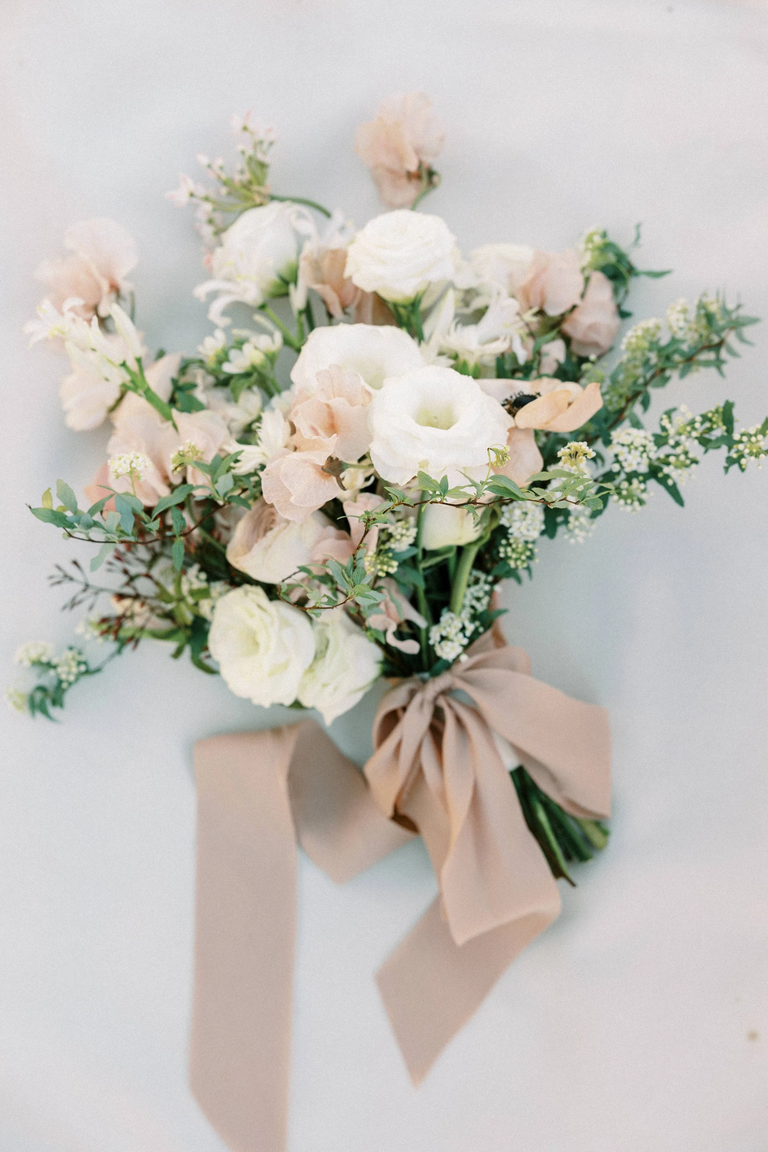 A bouquet of white and blush pink flowers tied with a beige ribbon.