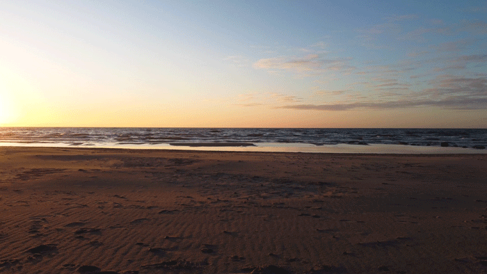 Good News Baptist Church Grand Rapids Michigan Lake Michigan Beach at sunset with sand in the foreground, ocean waves, and a partly cloudy sky near dusk.