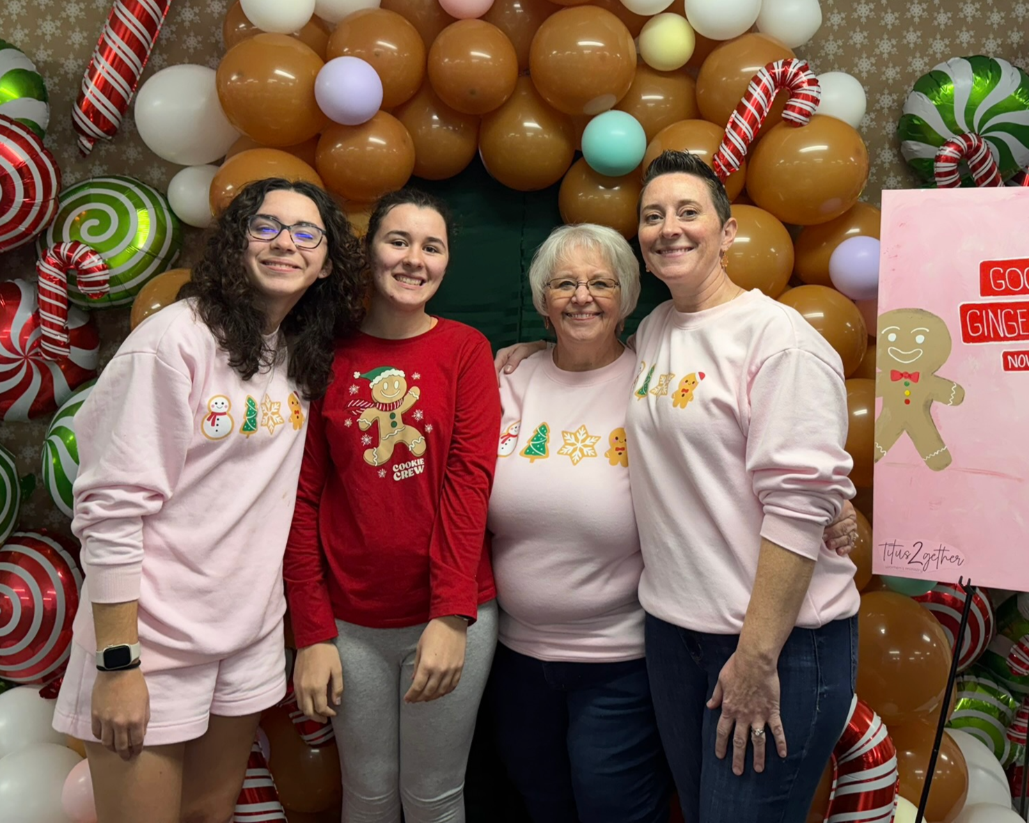 Good News Baptist Church Grand Rapids Michigan Four women standing together, smiling, in front of a festive holiday balloon backdrop with Christmas-themed decorations and a pink sign that says 'Good Gingers November'.