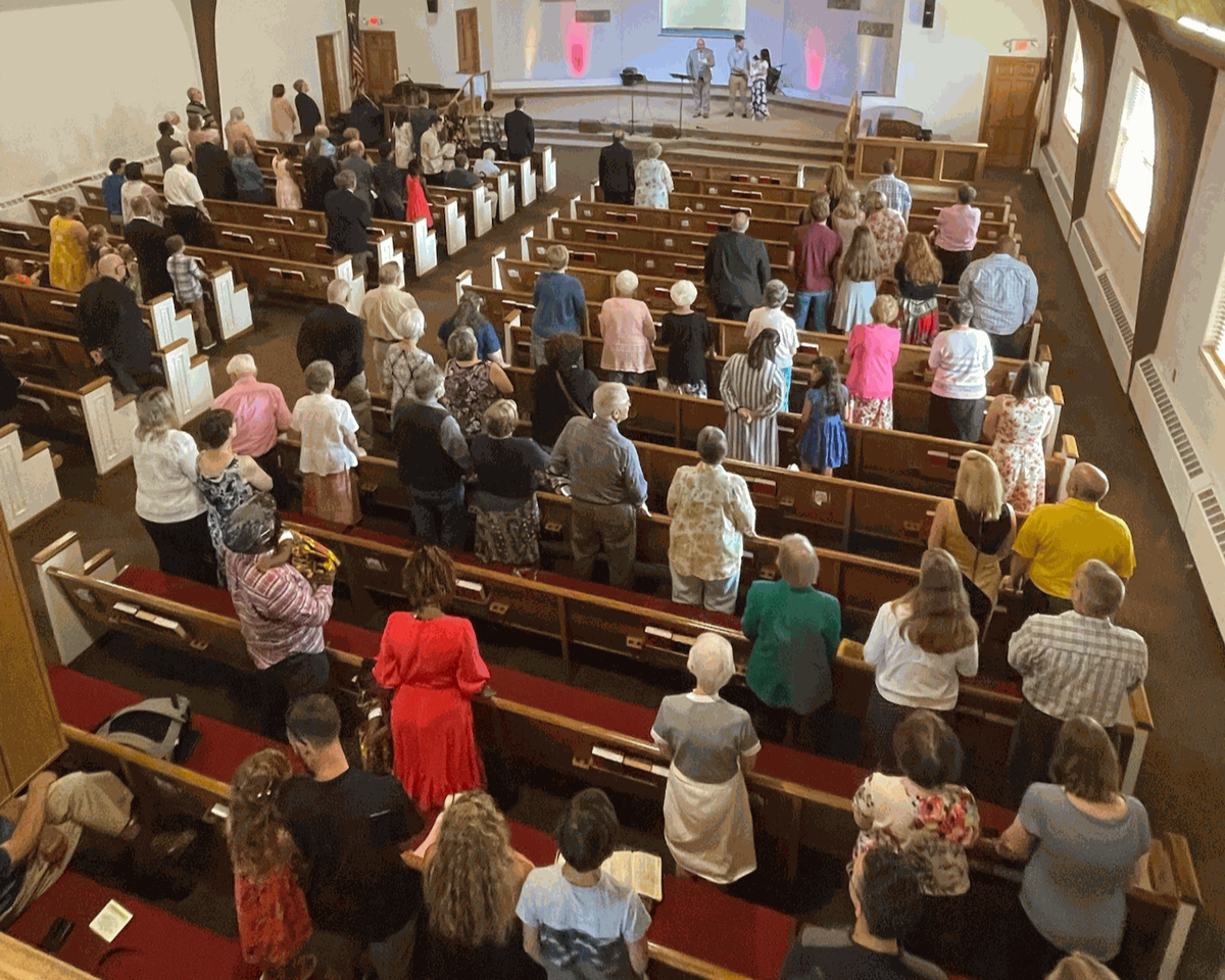 Good News Baptist Church Grand Rapids Michigan People gathered inside a church for a service or event, some standing in pews and others at the front by the stage.