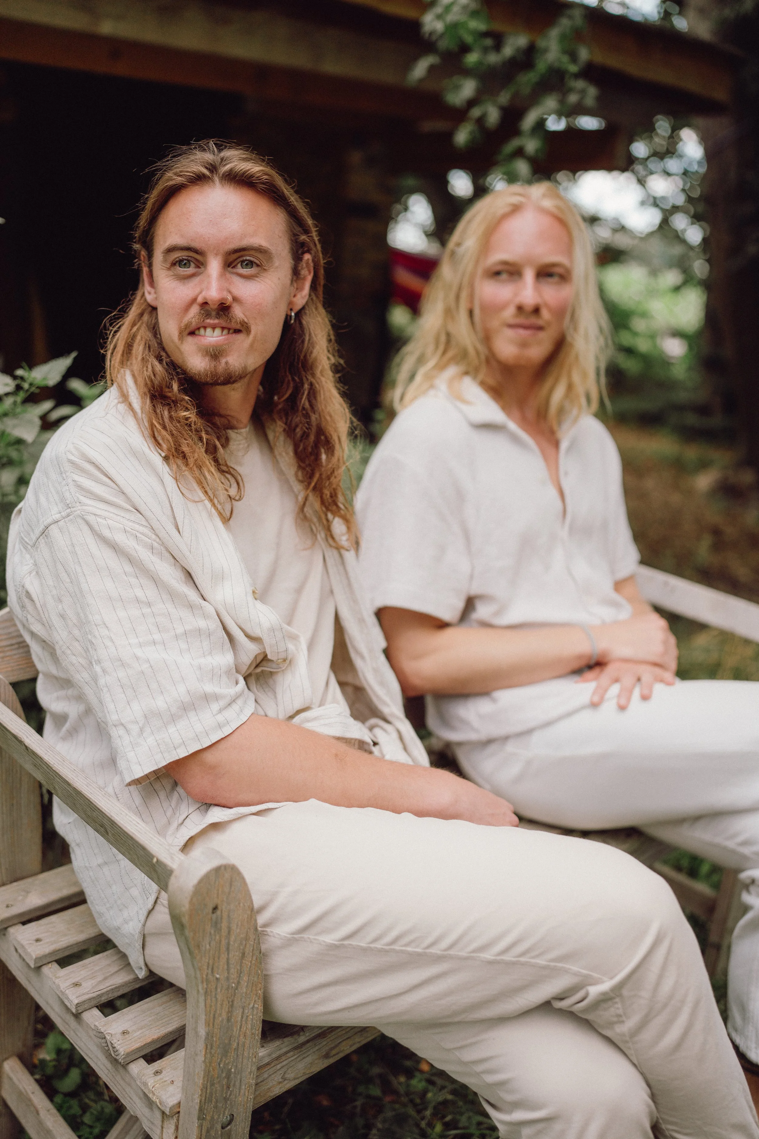 Zwei Frauen sitzen auf einer Bank im Freien, umgeben von Bäumen.