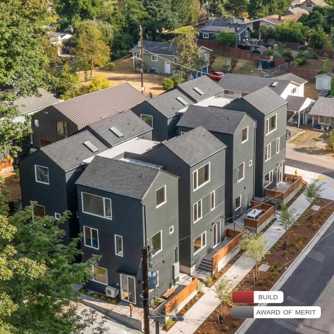 Aerial view of a modern black multi-unit residential building with multiple floors, surrounded by sidewalk and trees in a suburban neighborhood.