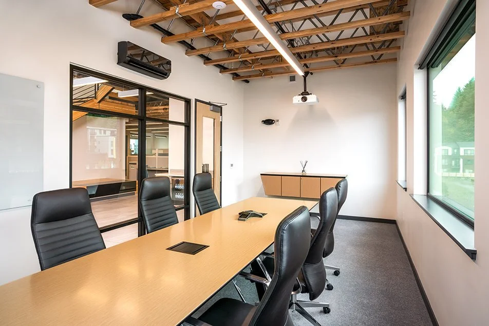 Conference room inside the 98th Avenue Office Building, showing a long meeting table, chairs, exposed ceiling structure, and projector.