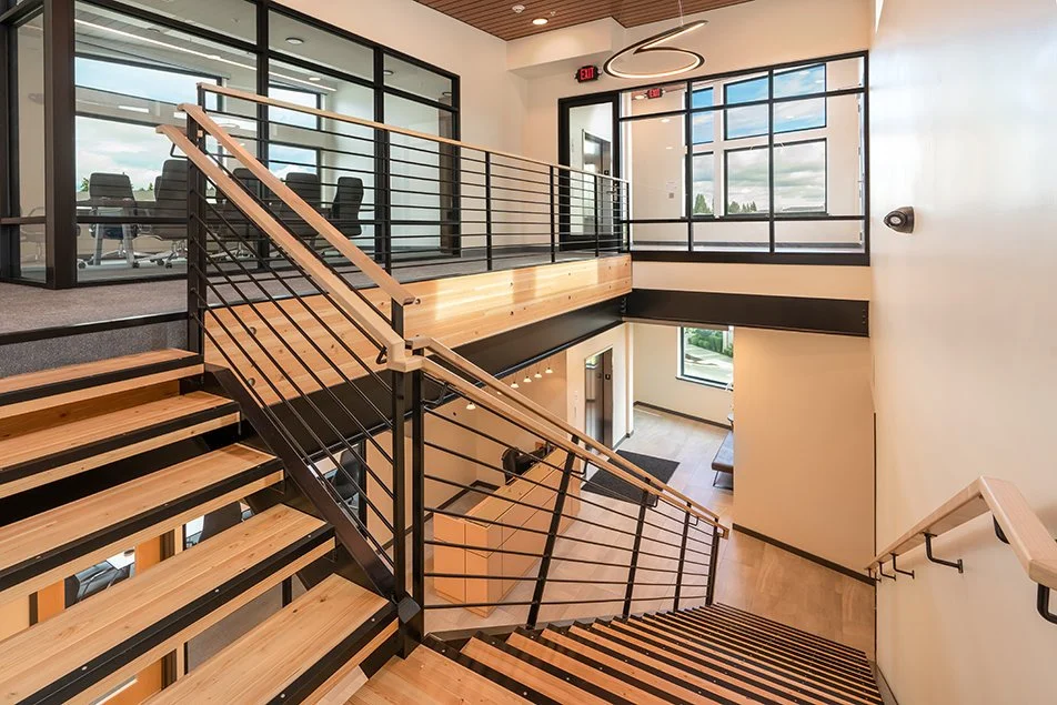 Interior stairwell showing wood steps, steel railings, and the upper landing with large windows.