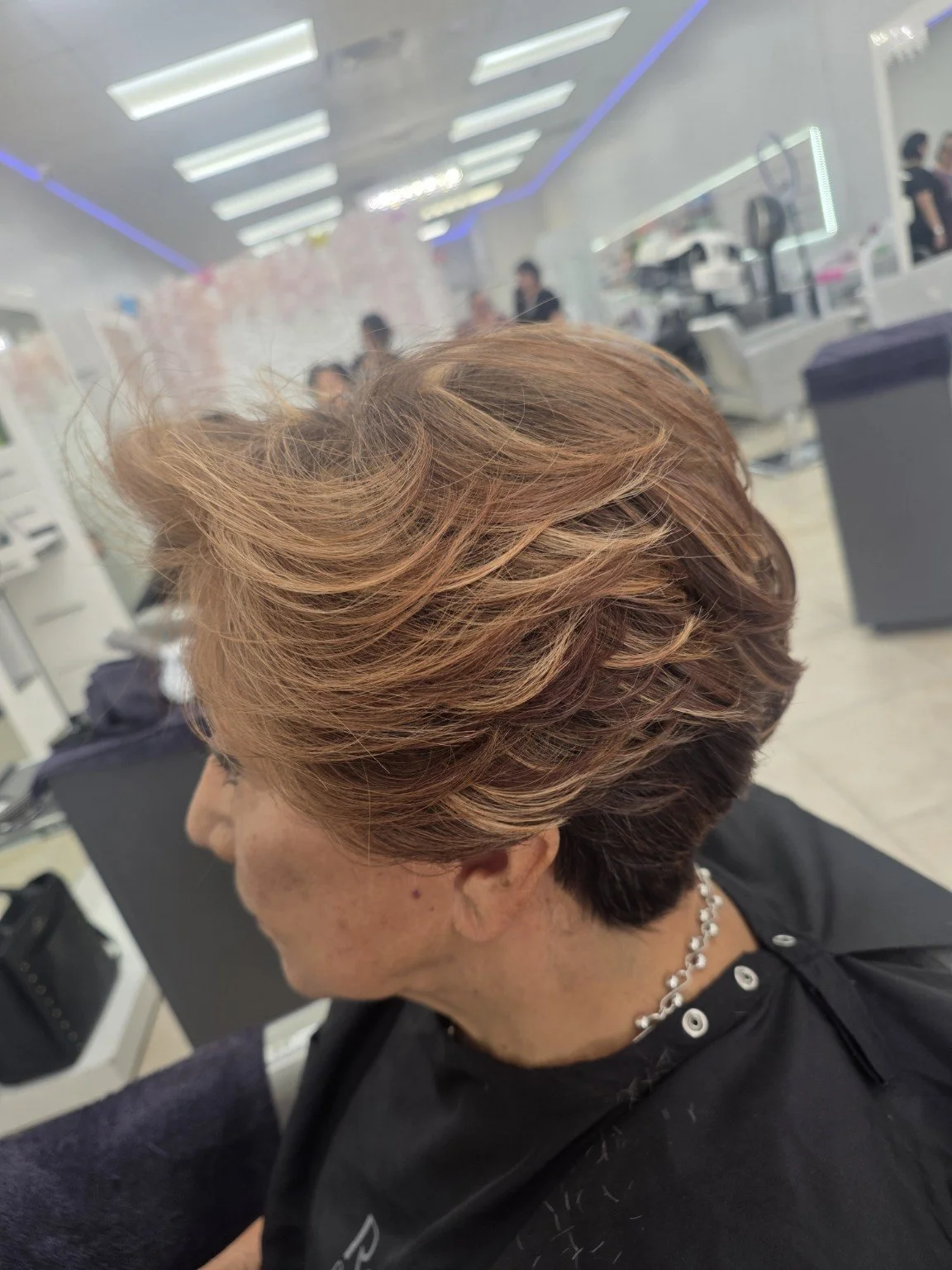 Side view of a woman with short, layered, auburn hair in a salon.